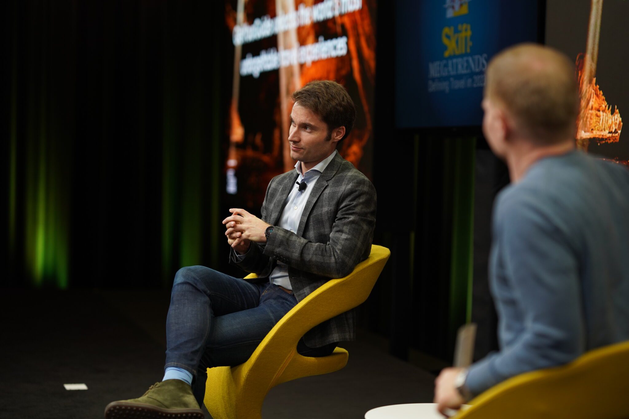 Two men sitting in chairs on a conference stage.