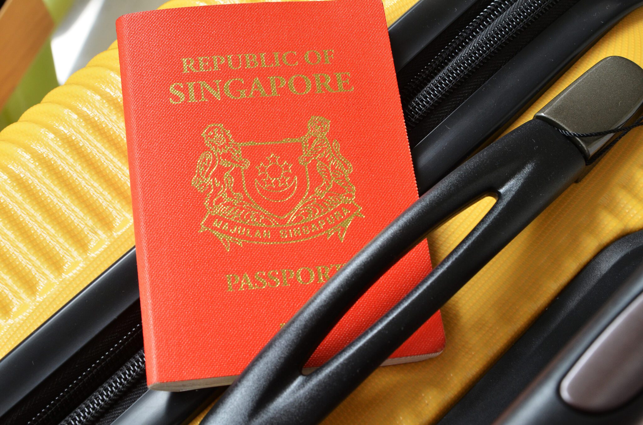 A Singaporean passport sitting atop a yellow suitcase.