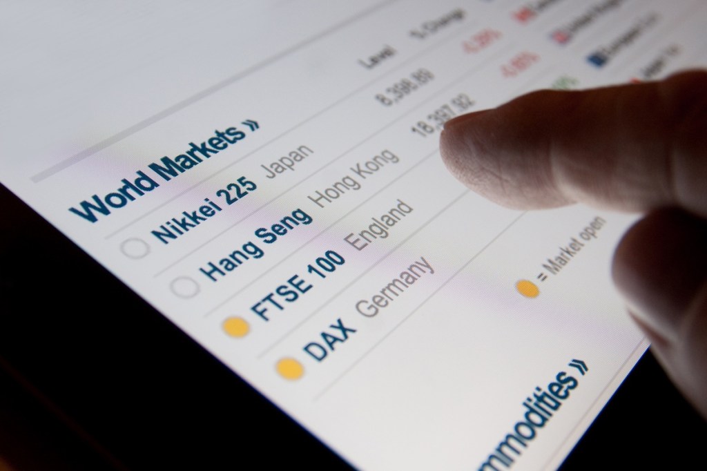 A finger hovering over a screen listing world markets.