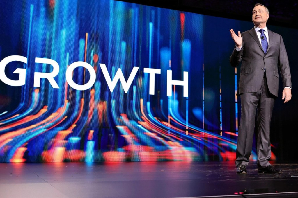 CEO speaking on stage with the words Growth on the screen behind him