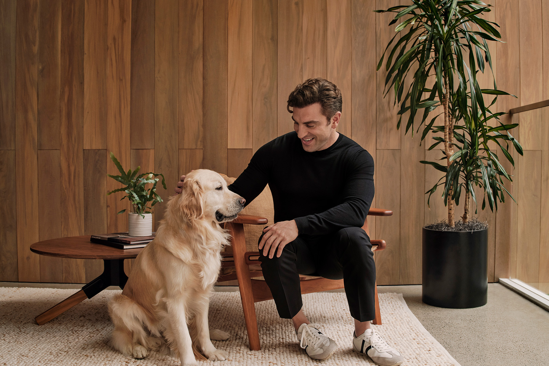 Portrait of a man dressed in black sitting on a chair next to a dog