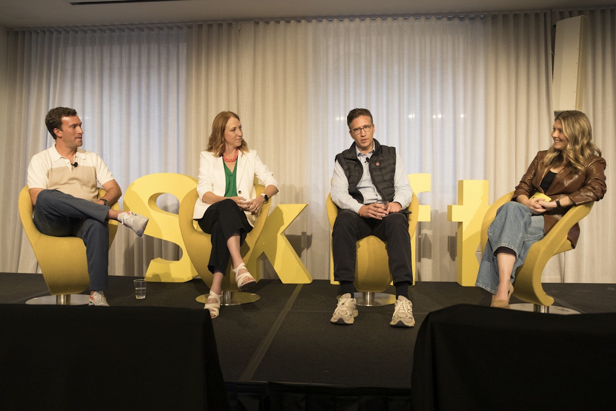 Four people speaking on stage while seated on yellow chairs.