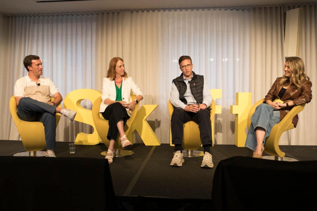 Four people speaking on stage while seated on yellow chairs.