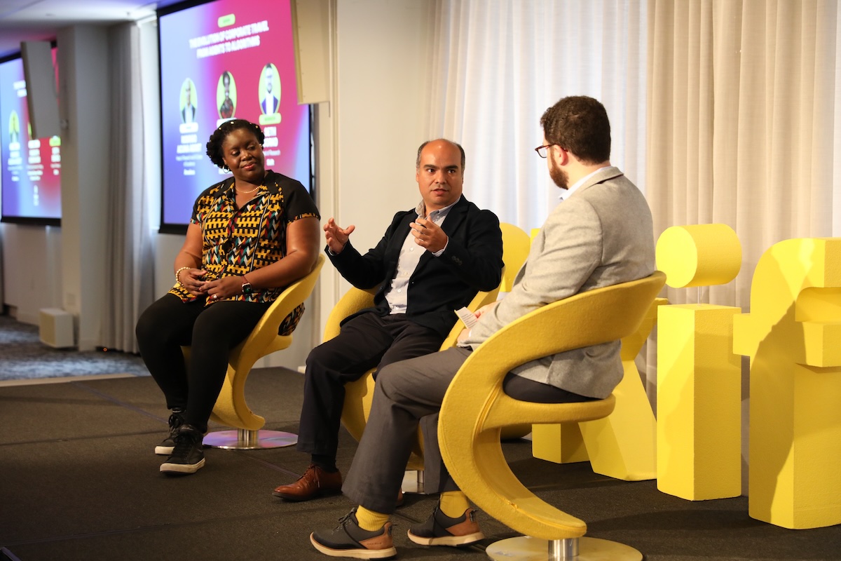 A woman and two men sitting and talking on stage at a conference.