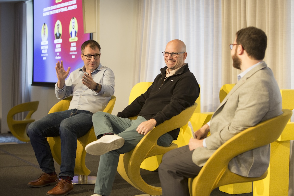 3 men sitting on yellow chairs on stage at a Skift conference.