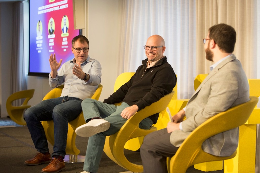 3 men sitting on yellow chairs on stage at a Skift conference.