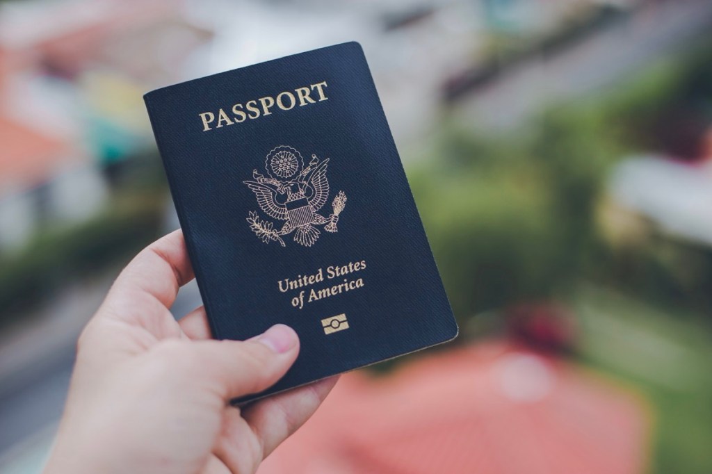 One single hand holding a blue American passport in front of a blurry background