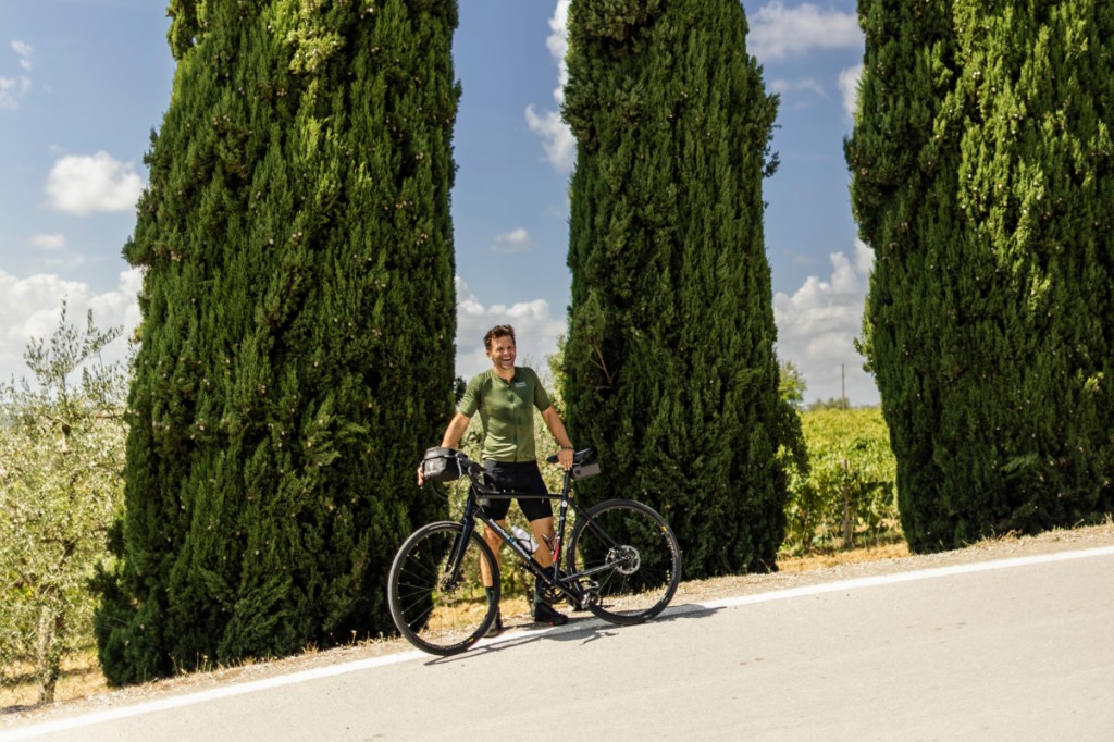 A man on his racing bike with the Tuscan background and distinctive pine trees behind him