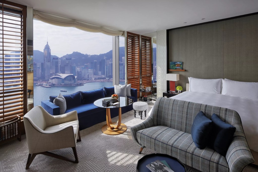 a view of a luxurious guest room at the Rosewood Hong Kong Hotel, with a view of the Hong Kong skyline and a king bed