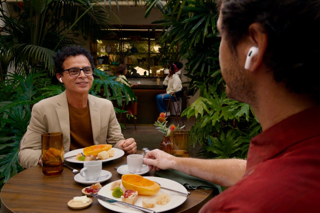 Two people sitting at a table and talking while wearing AirPods.