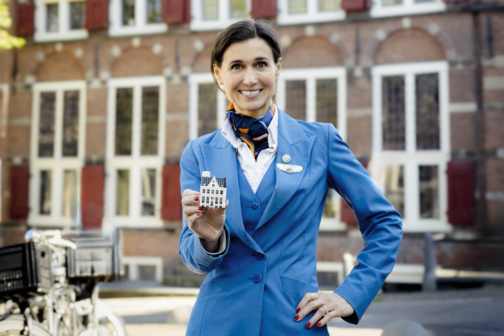 A flight attendant holding a miniature Delft Blue house., which business class travelers on KLM flights receive.