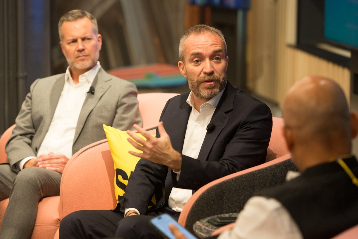Three men in chairs speak on a stage.