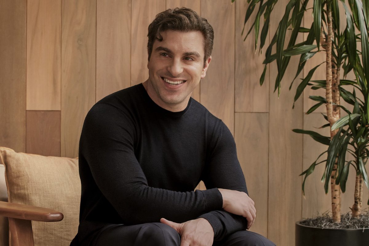 A man sitting in a chair wearing a black shirt. His arms are partially folded.