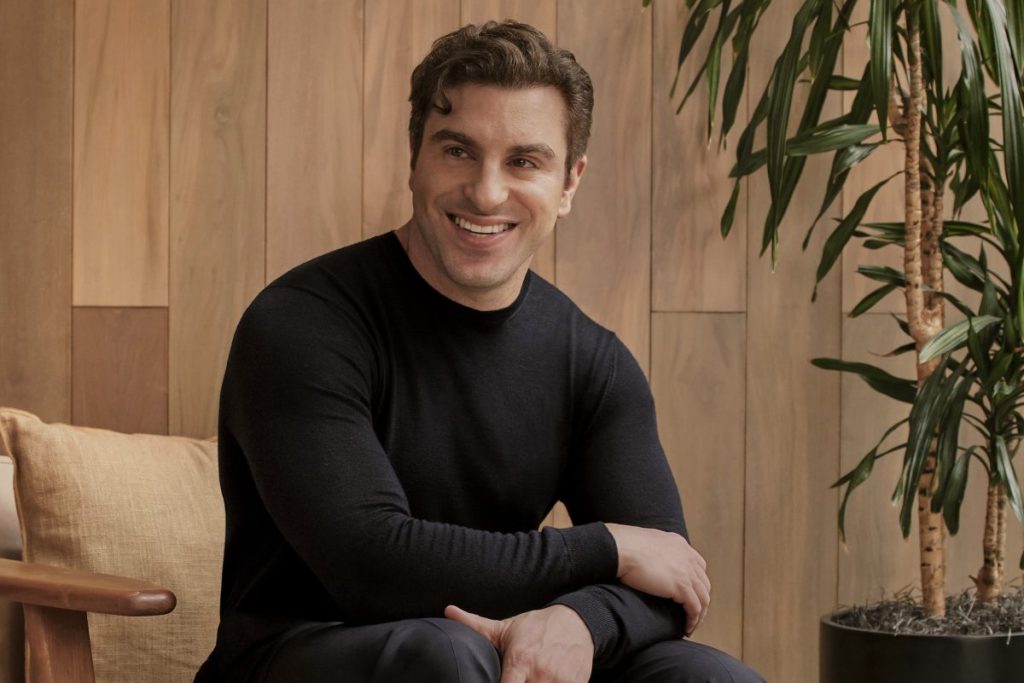A man sitting in a chair wearing a black shirt. His arms are partially folded.