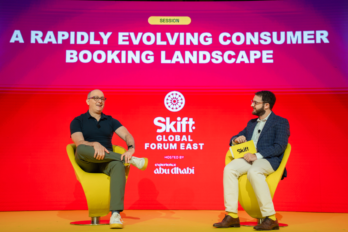 Two men sitting in yellow chairs on stage at Skift Global Forum East.