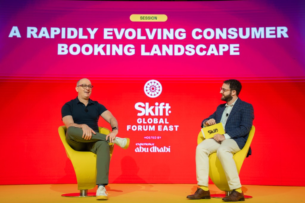 Two men sitting in yellow chairs on stage at Skift Global Forum East.