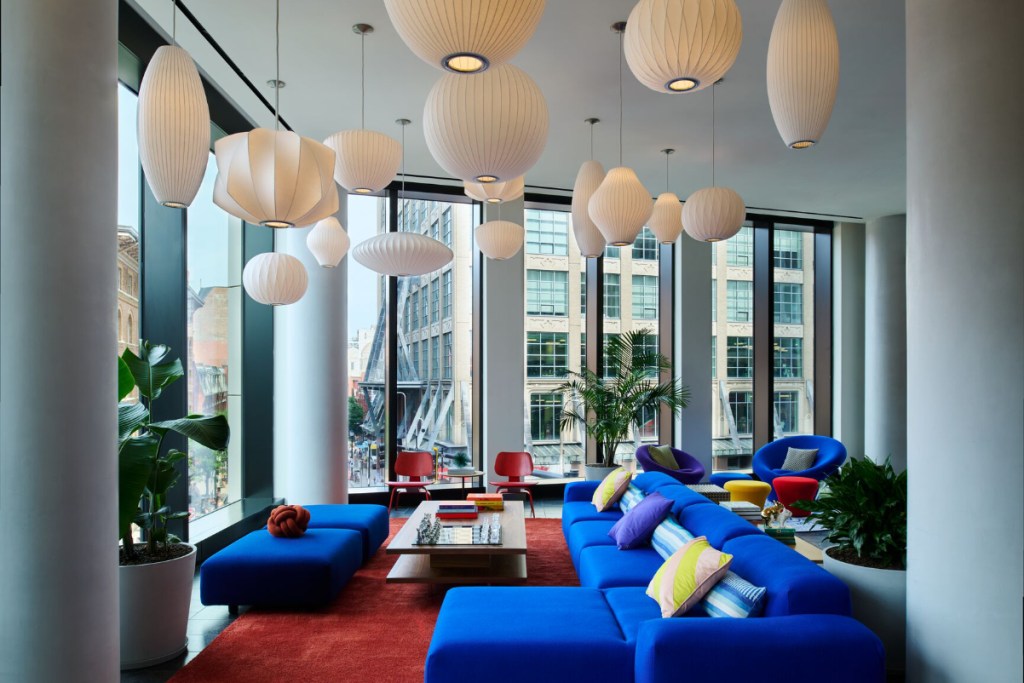 Image of a hotel lobby with a lot of colorful cobalt blue couches, bright red rugs, and unusually shaped pendant lamps from the ceiling