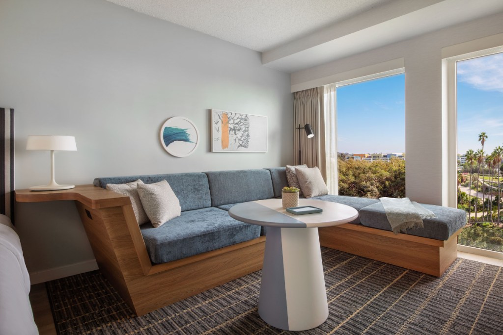 Image of a high-end sofa and shoes with distinctive furniture, with big windows overlooking a sunny day and a park with palm trees in California.