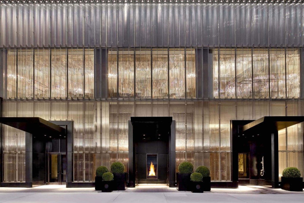 Image of the front of a Baccarat Hotel in New York City with a lot of glittering jewel tones and the view of a fireplace through a doorway on a bright sunny day