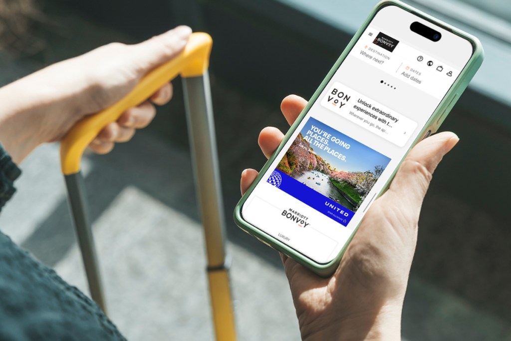 Image of a traveler's hand holding a Marriott Bonvoy app open to an ad from United Airlines, placed as part of Marriott Media.