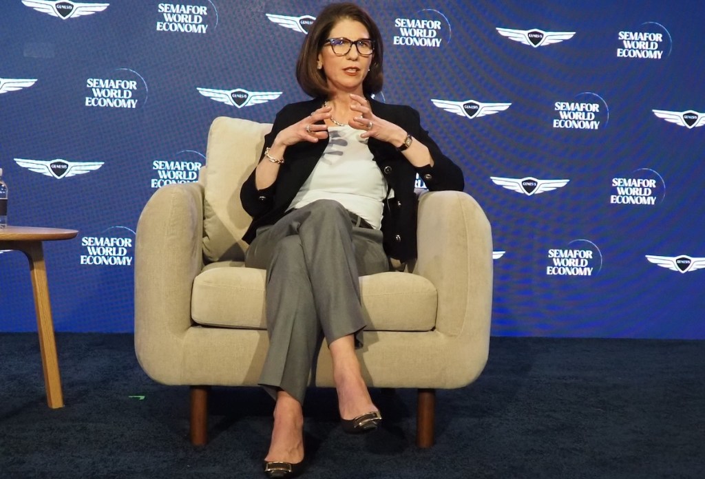A woman sitting cross-legged on a wide chair on a conference stage.