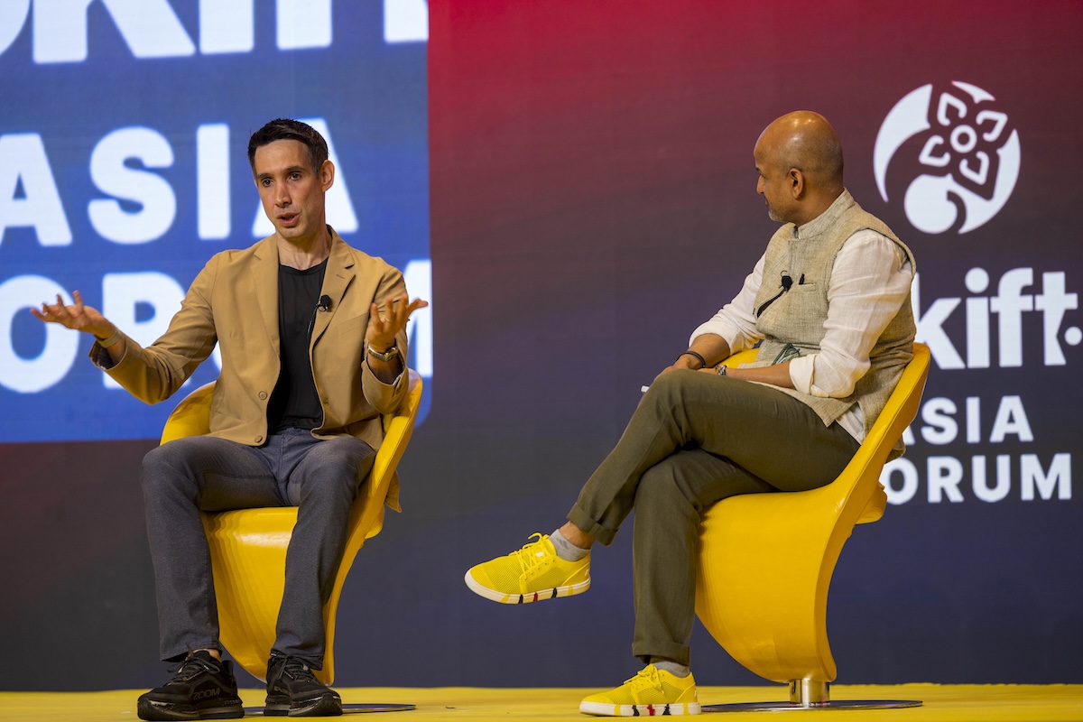 two men sitting on stage, one is a sport coat and one wearing a vest.