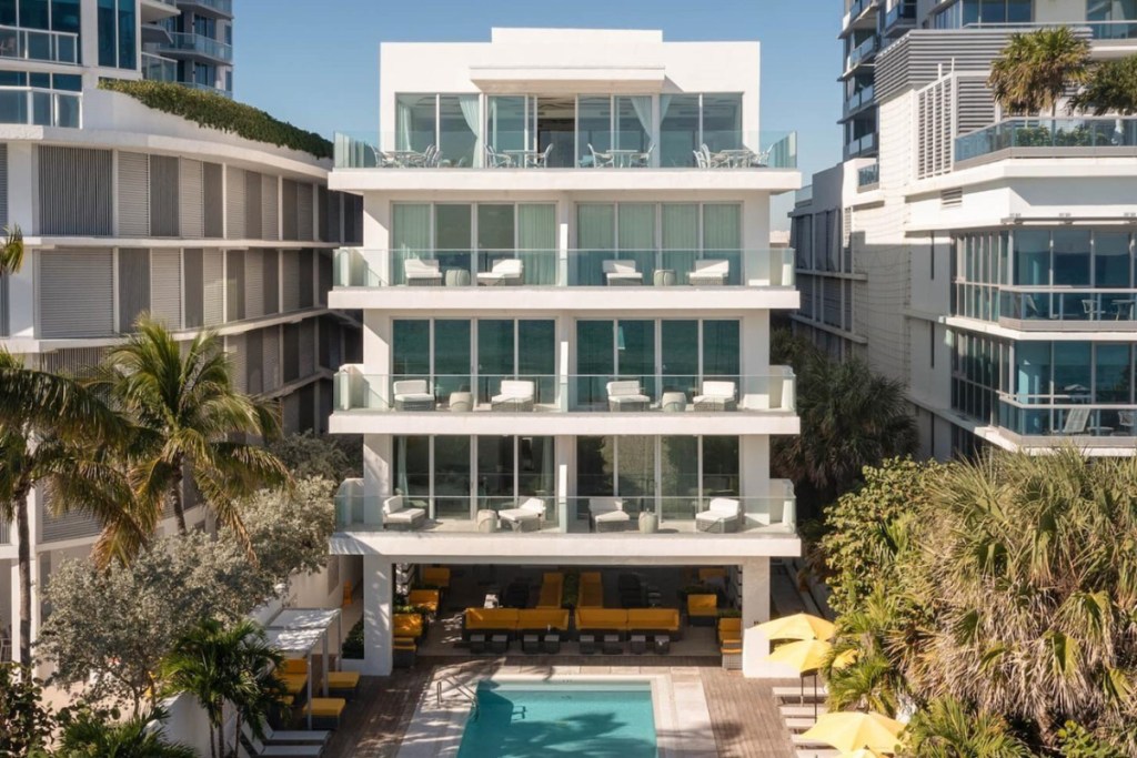 exterior of a Miami Beach hotel with an outdoor pool and lots of beach chairs on a sunny day