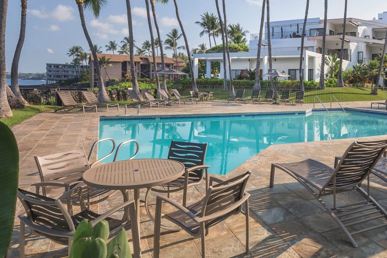 Image of a palm tree and swimming pools next to a timeshare resort on a sunny day.